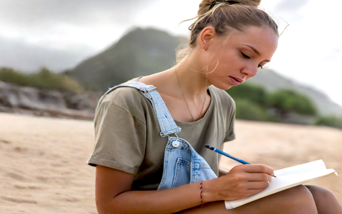 Young woman journaling by hand on the beach, embracing a quiet moment of slow living and reflection.