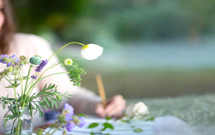 Young woman writes a handwritten card in the garden, embracing a quiet moment of slow living and reflection.